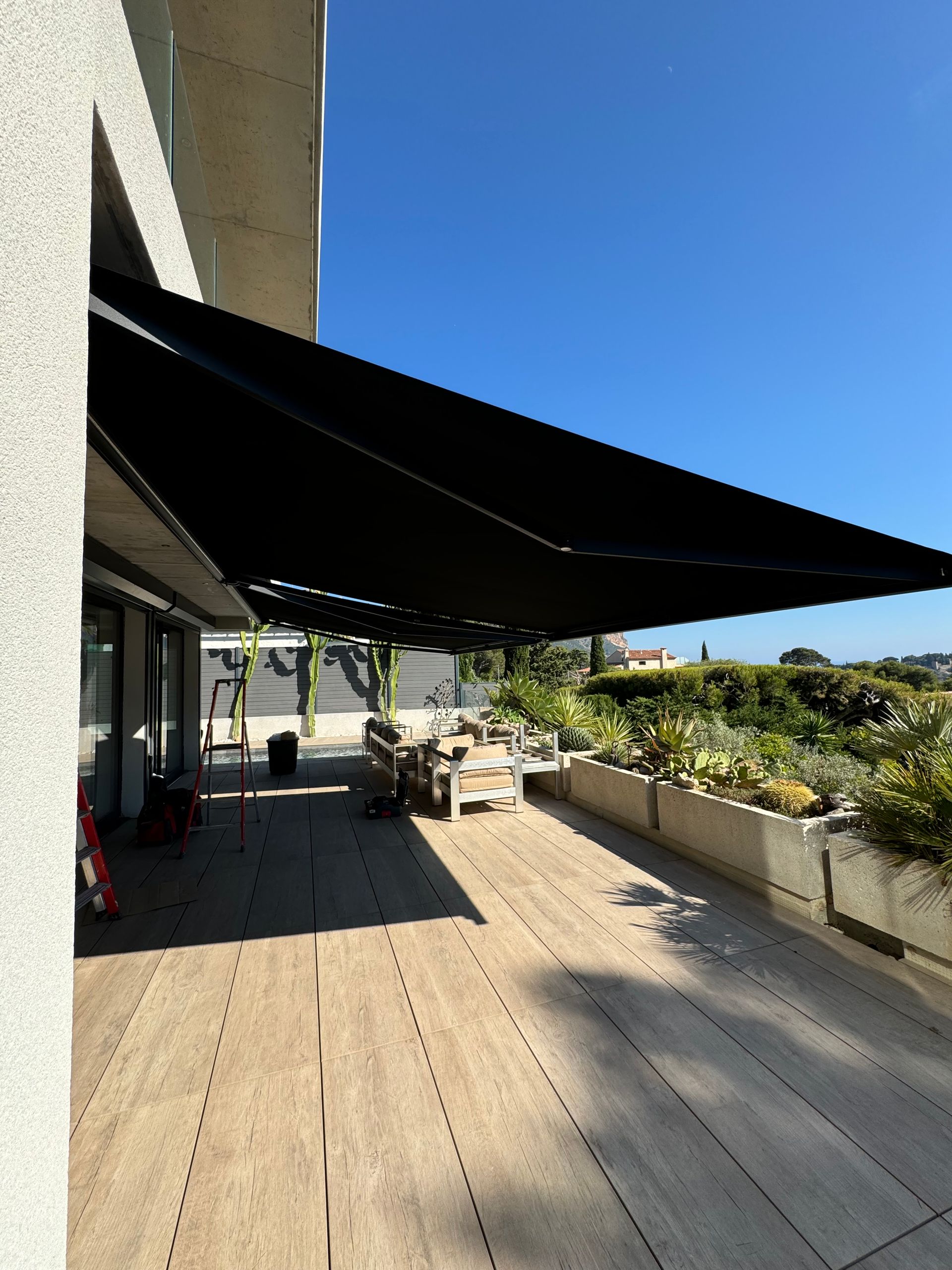 Une terrasse en bois abrité par un grand store banne noir