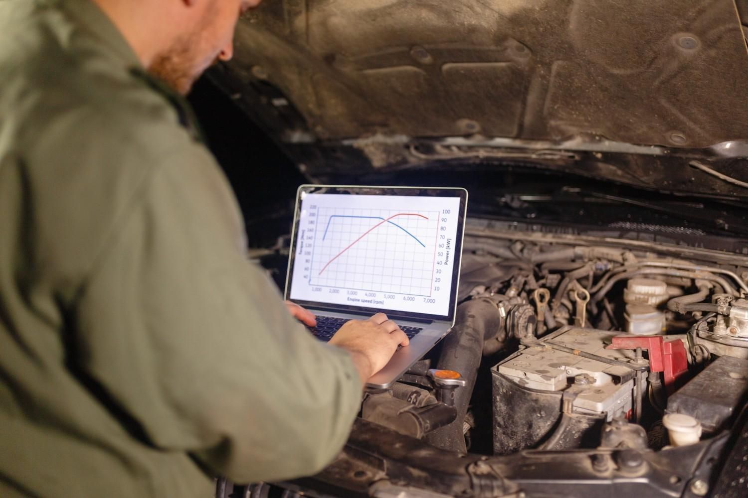Persona que utiliza una tableta para diagnosticar el motor de un coche con el capó abierto.