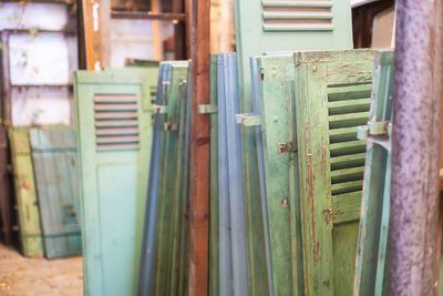 Une rangée de volets de fenêtre anciens en bois vieilli, dans des tons de bleu pâle et de vert, entreposés dans un entrepôt.