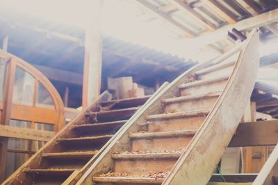 Escaliers en bois à l'intérieur d'un vieux bâtiment rustique avec charpente apparente et rampes en bois.
