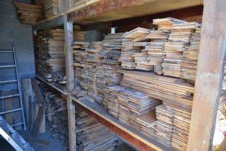 Dans un atelier, des étagères en bois sont remplies de piles de bois de construction et de planches.