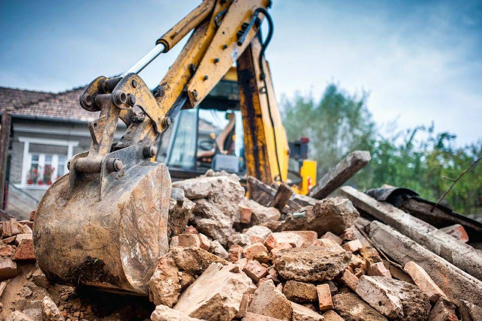 Au premier plan, un godet jaune d'excavatrice est en équilibre précaire au-dessus d'un tas de briques.