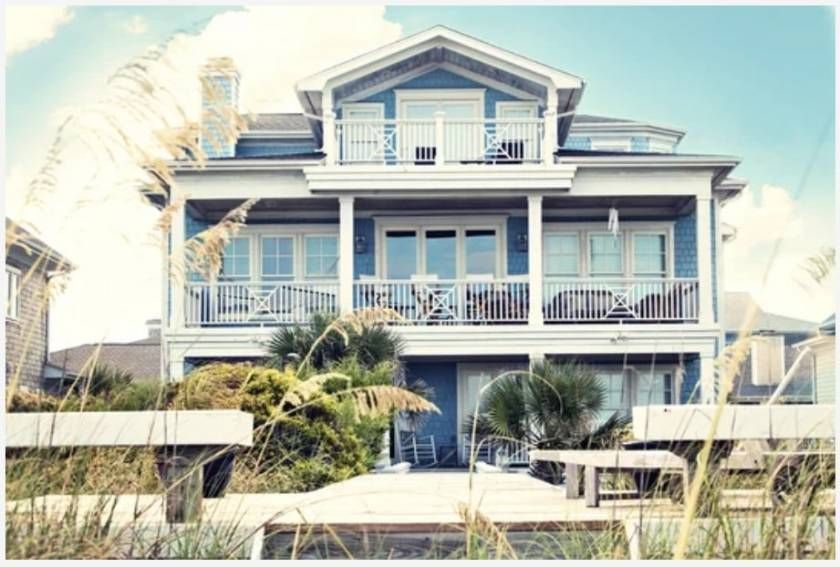 Blue beach house with balconies, set among greenery and tall grass.