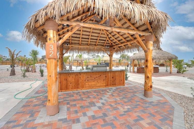 Tiki-style outdoor kitchen with wood counter, barbecue, and thatched roof under a blue sky.