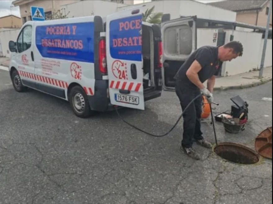 Hombre con una manguera trabajando en un pozo al lado de una camioneta de servicio blanca.