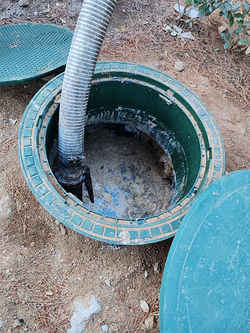 Tanque séptico siendo bombeado; tapa verde, manguera insertada, sucio por dentro.