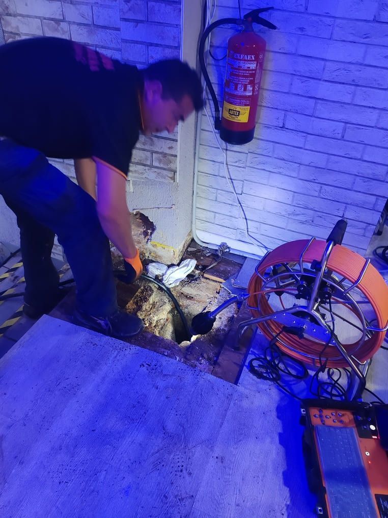 Hombre inspeccionando un desagüe con una cámara. Extintor en la pared, luz azul.
