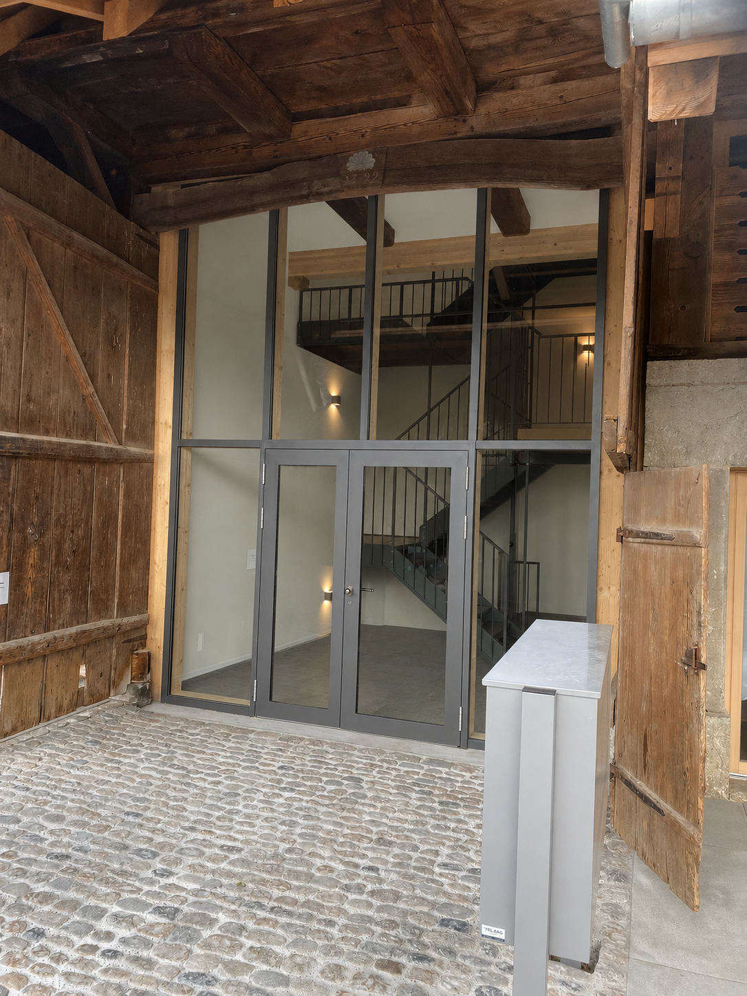 Holzfassade mit grossen Fenstern, Backsteinverkleidung und überdachter Veranda unter einem roten Dach.