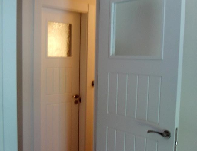 Una puerta blanca con una pequeña ventana en un pasillo.