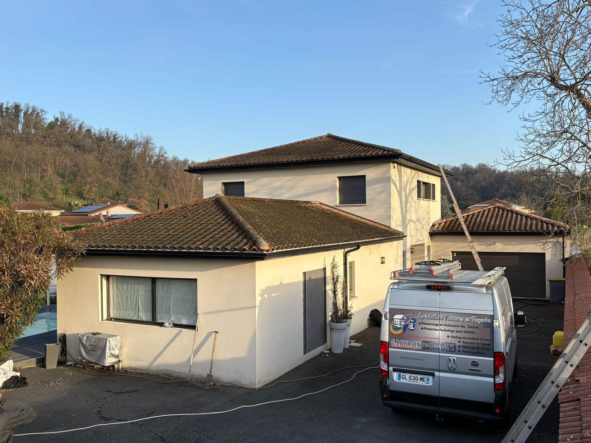 Une camionnette de chantier garée devant une maison beige à deux étages avec un toit de tuiles brunes.