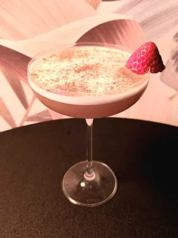 Un cóctel servido en una copa tipo coupe con tallo, adornado con una frambuesa y espolvoreado con especias