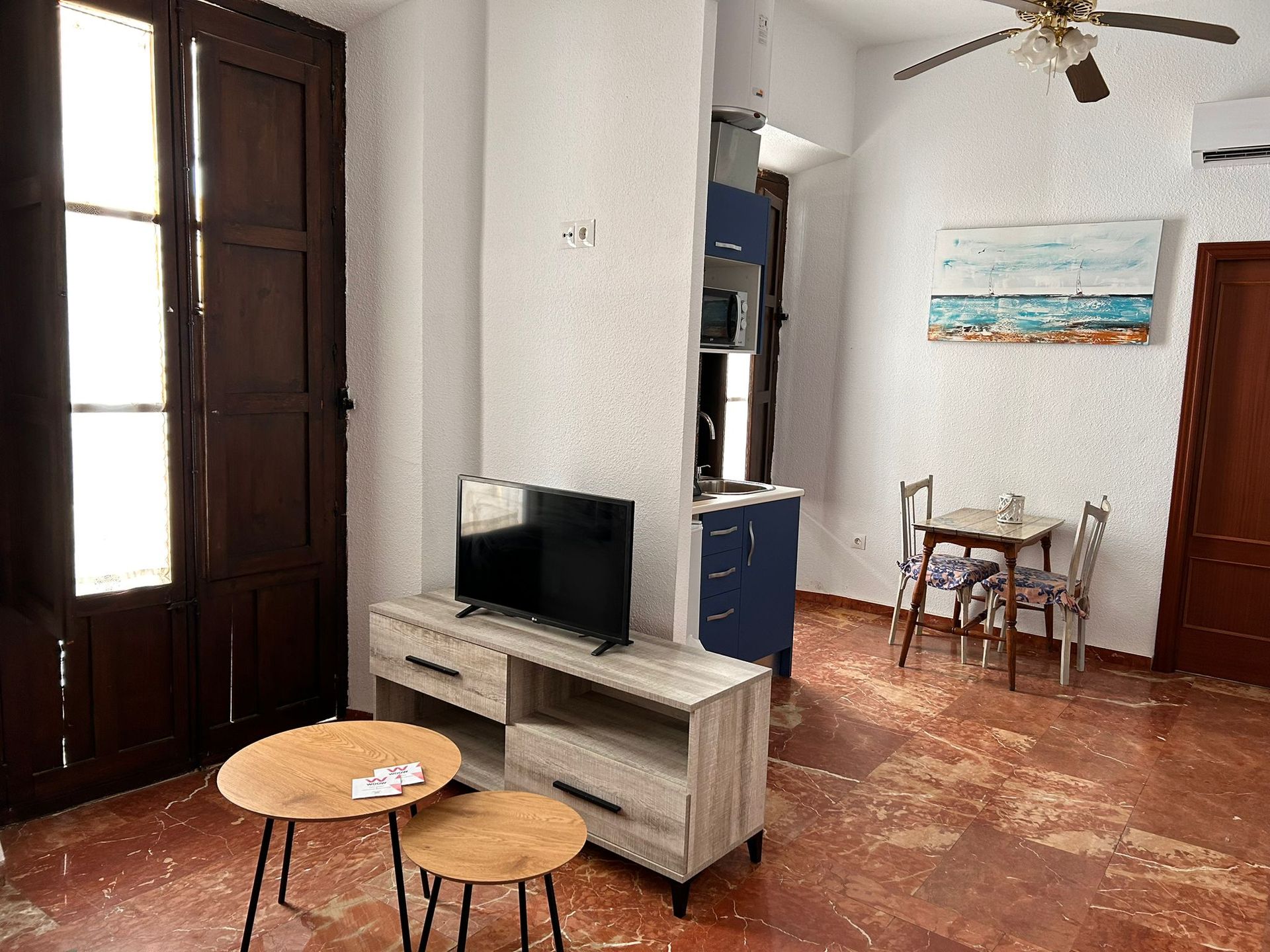 Una sala de estar con televisor de pantalla plana, mesas, sillas y ventilador de techo.