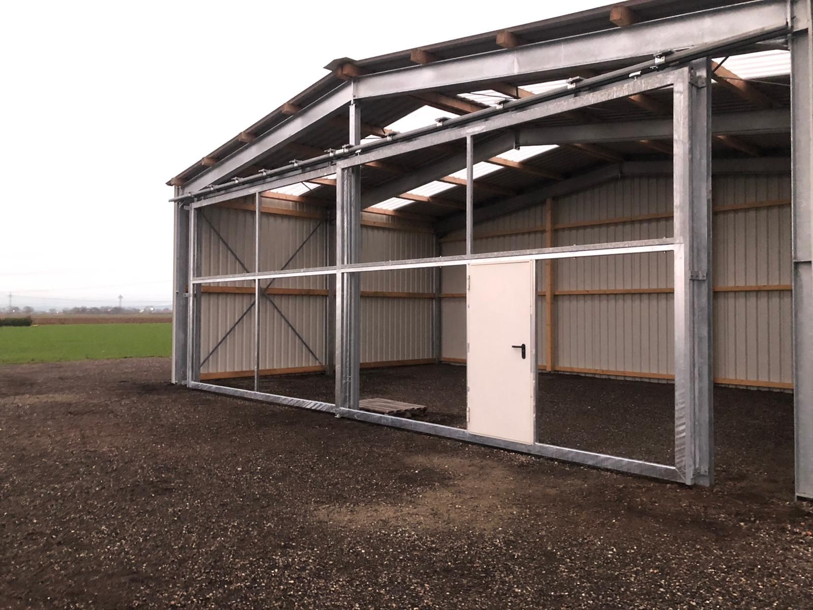 ein großes Metallgebäude mit einer Tür mitten auf einem Feld.