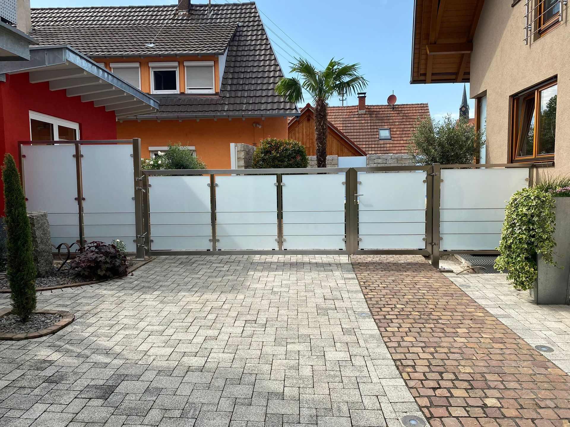 eine gemauerte Auffahrt mit einem Zaun und einem roten Haus im Hintergrund