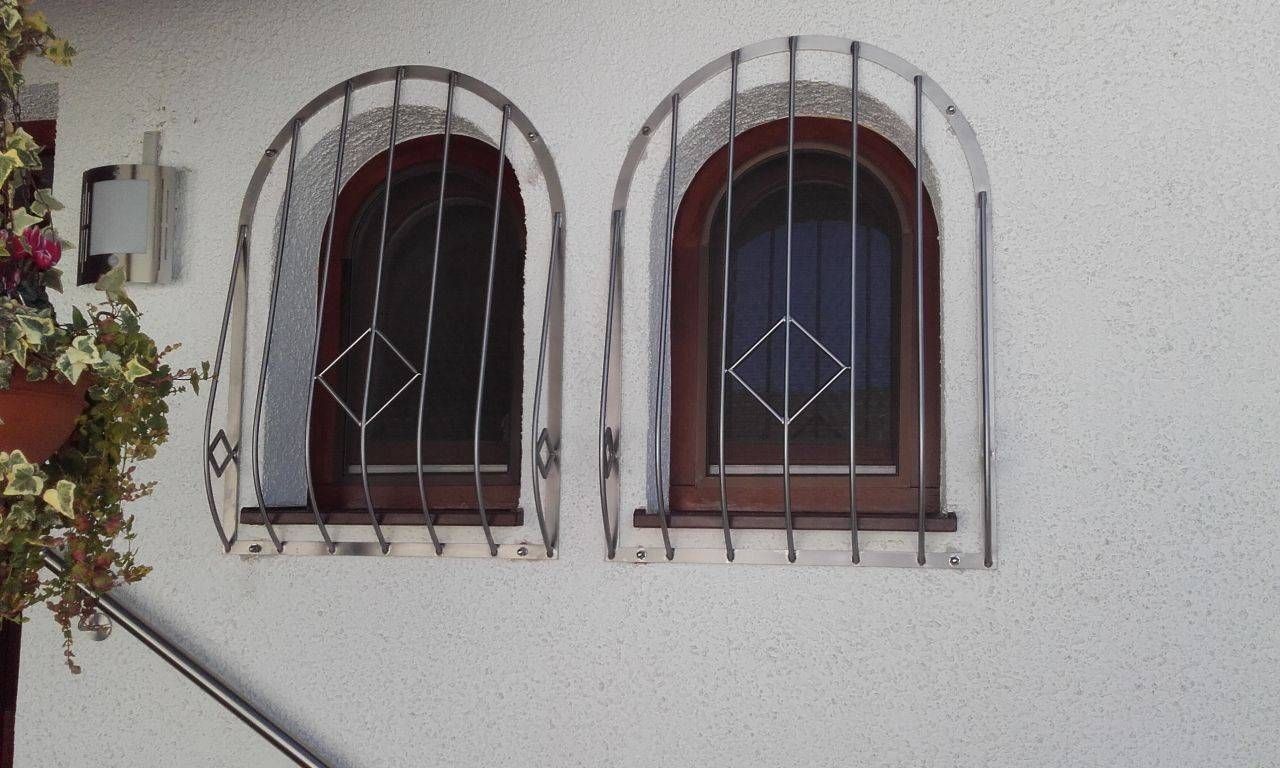 Zwei Bogenfenster mit schmiedeeisernen Gittern an einer weißen Wand