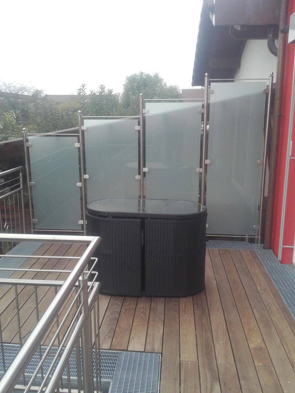 ein Balkon mit einem Korbtisch und einem Geländer aus Edelstahl