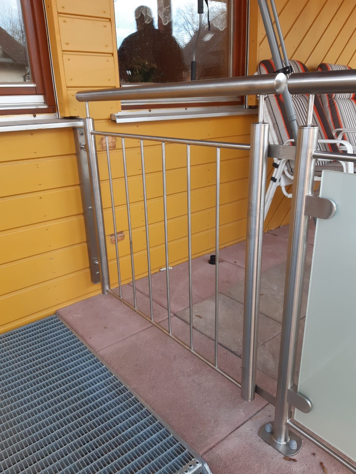 ein Edelstahlgeländer auf einem Balkon neben einem Fenster.