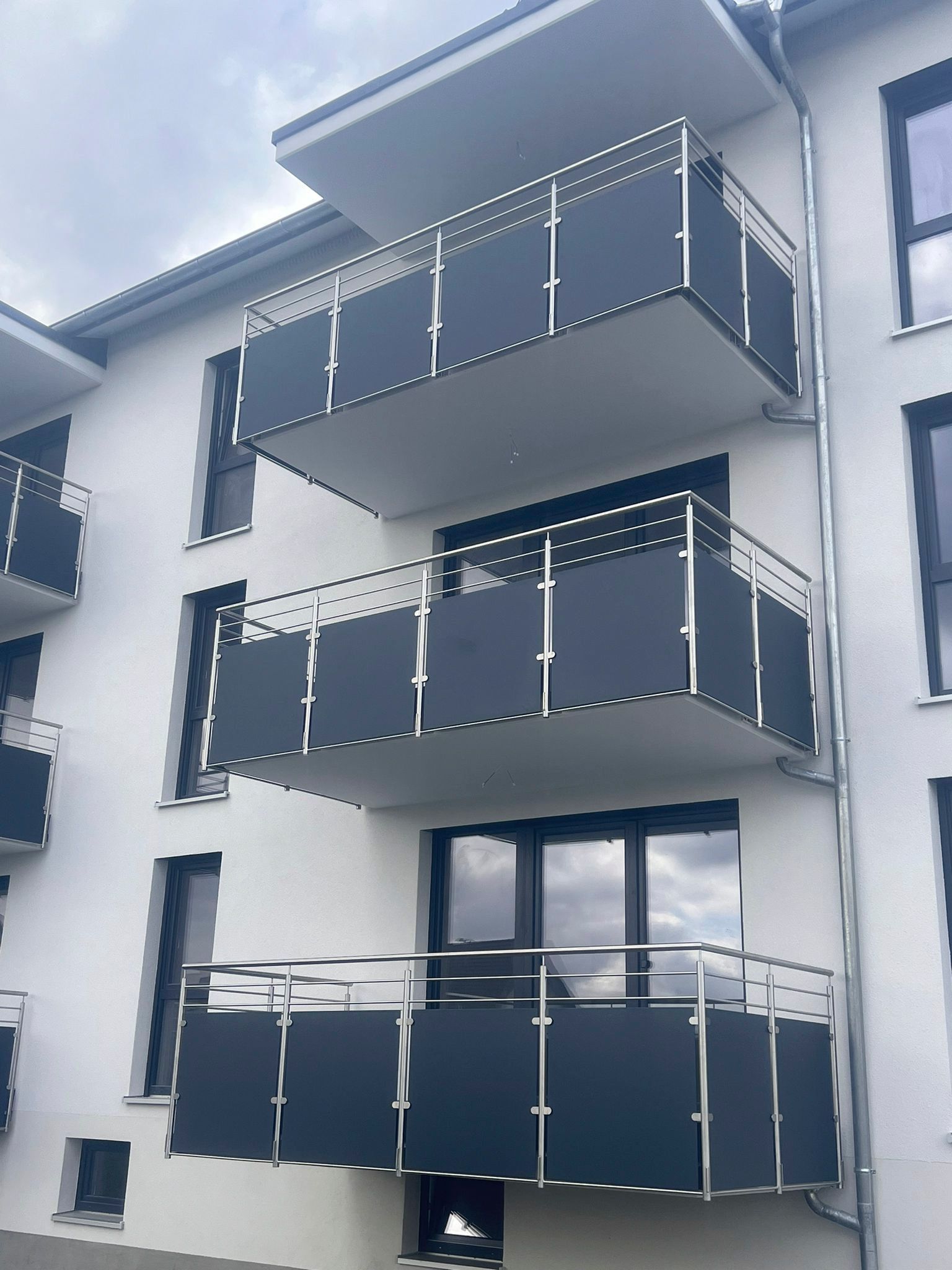 ein weißes Gebäude mit schwarzen Balkonen und Edelstahlgeländer