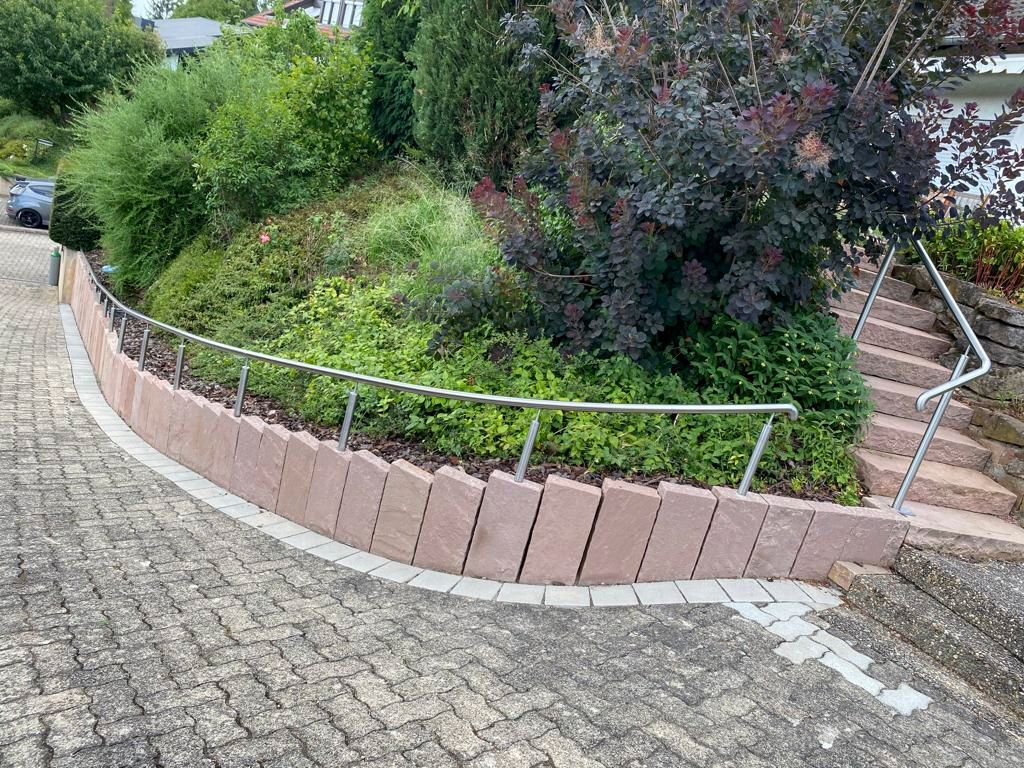 ein gemauerter Gehweg mit einem Edelstahlgeländer und einer Treppe, die zu einem Garten führt.