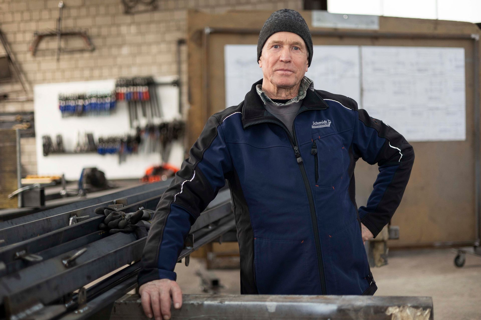 Ein Mann in blauer Jacke und schwarzem Hut steht in einer Werkstatt.