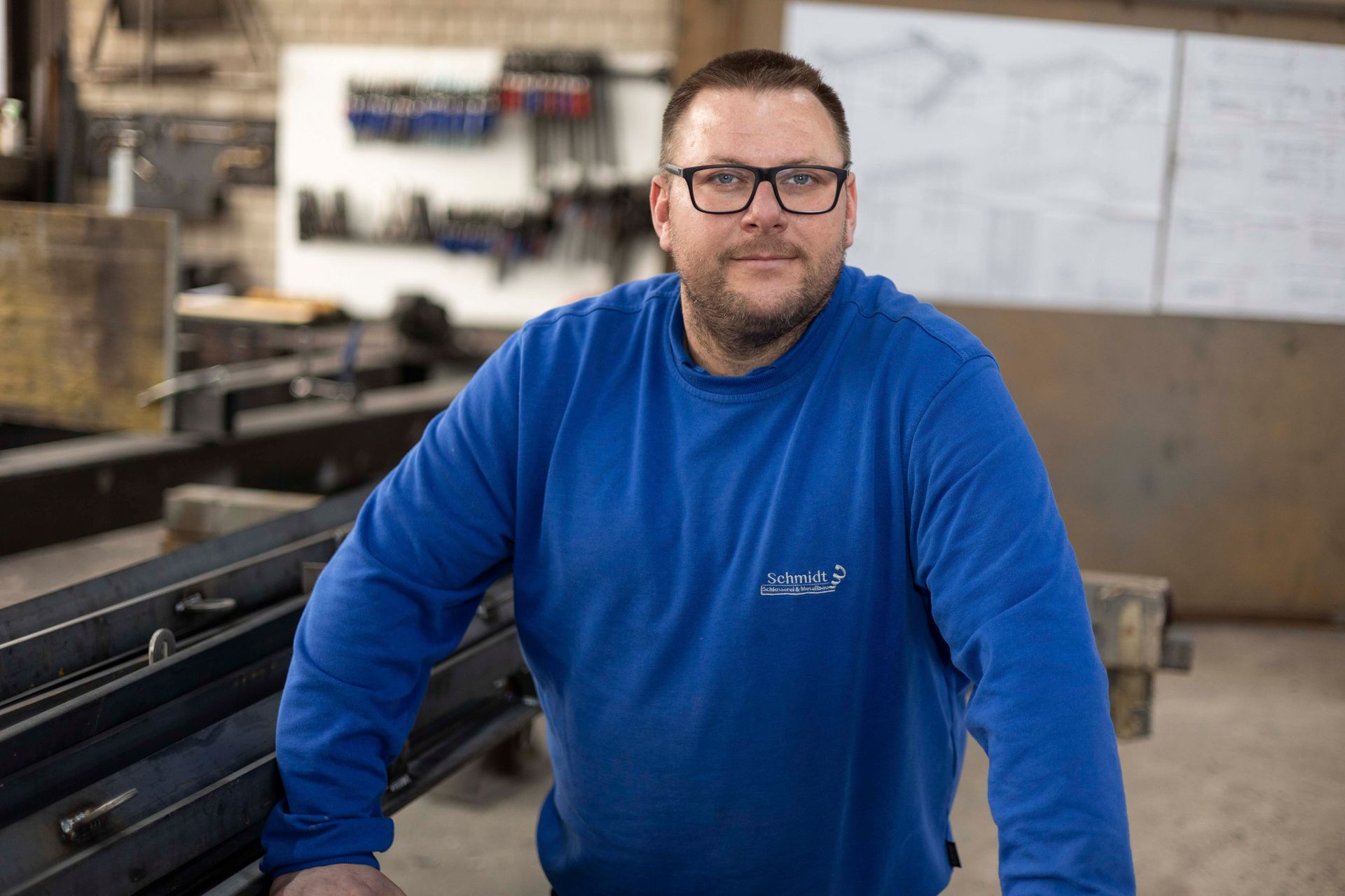 Ein Mann mit Brille und blauem Hemd steht in einer Fabrik.