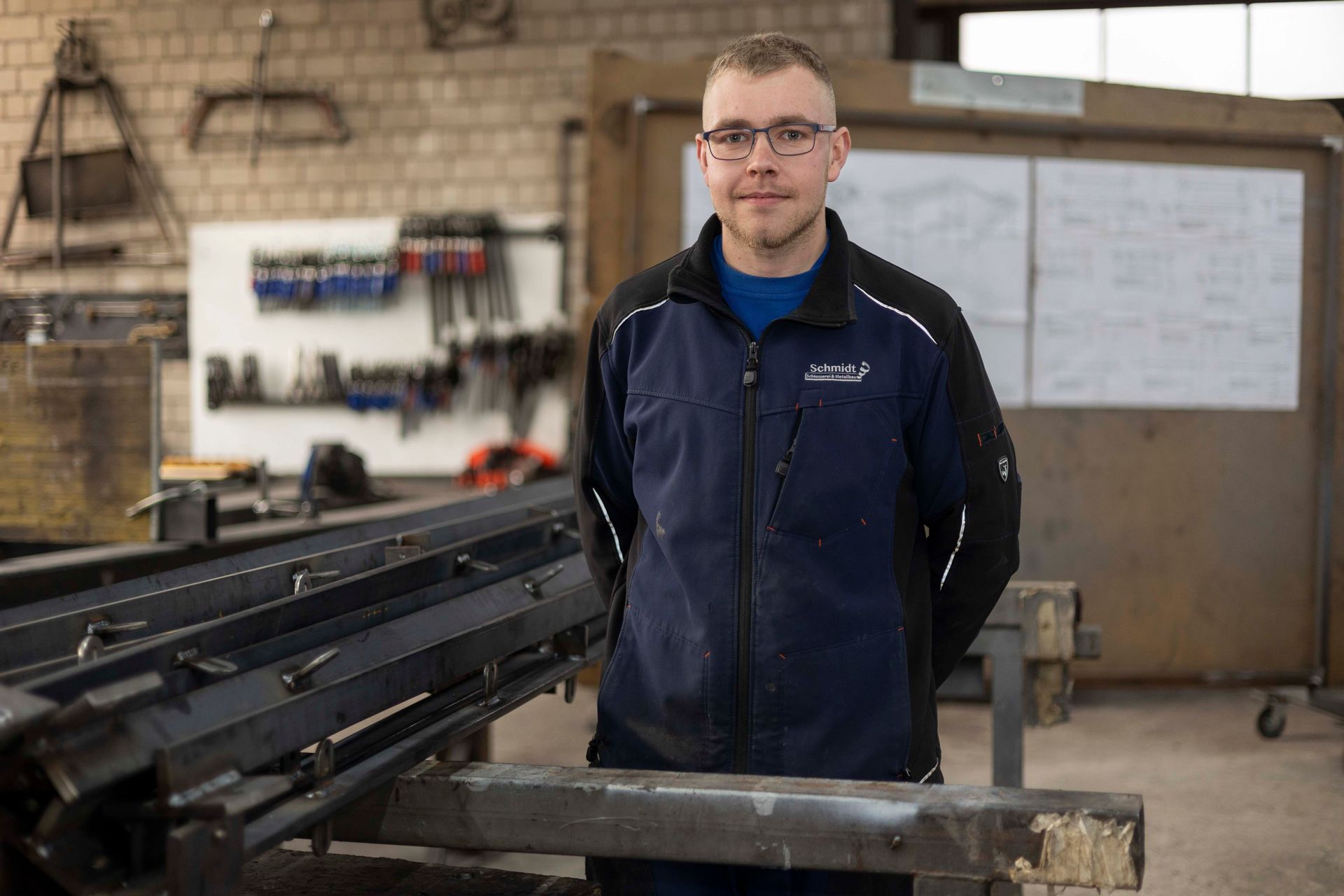 Ein Mann in blauer Jacke und schwarzer Hose steht in einer Werkstatt.