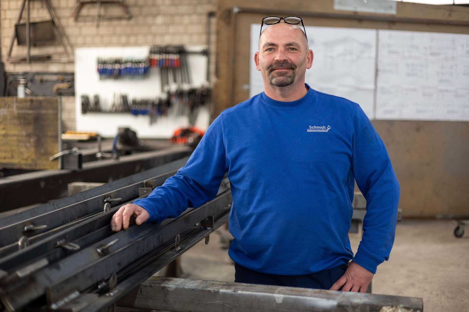 Ein Mann in einem blauen Hemd steht neben einem Metallträger in einer Fabrik.