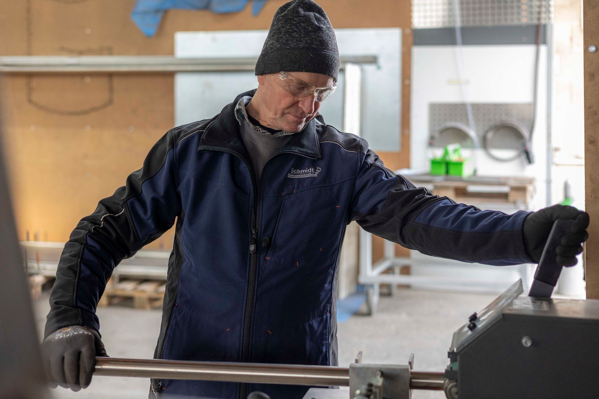 Ein Mann in blauer Jacke und schwarzen Handschuhen arbeitet an einer Maschine.