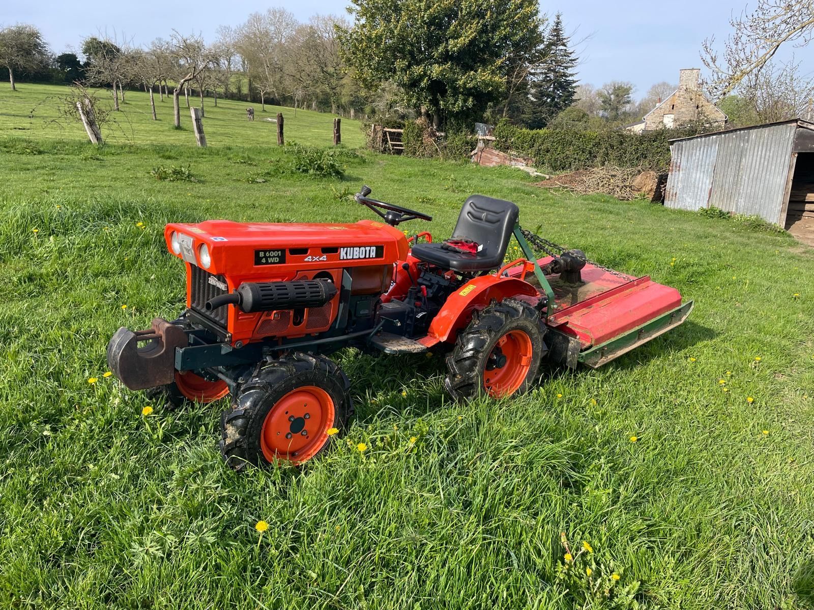 Tracteur tondeuse rouge Kubota stationné dans un jardin.