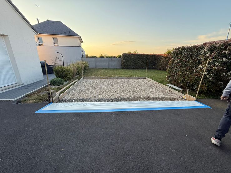 Création d’une zone en gravier avec coffrage en bois et bâche de protection devant une maison.