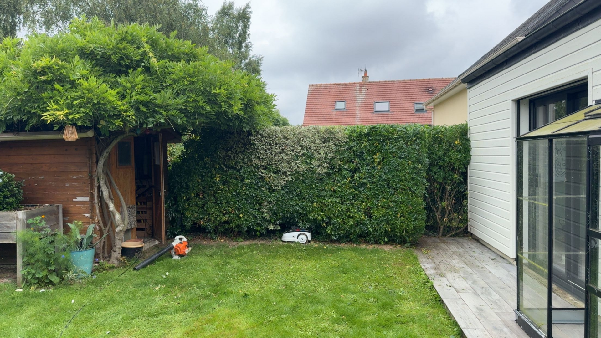 Extérieur de maison avec pelouse et arbres, espace vert calme en lotissement résidentiel.
