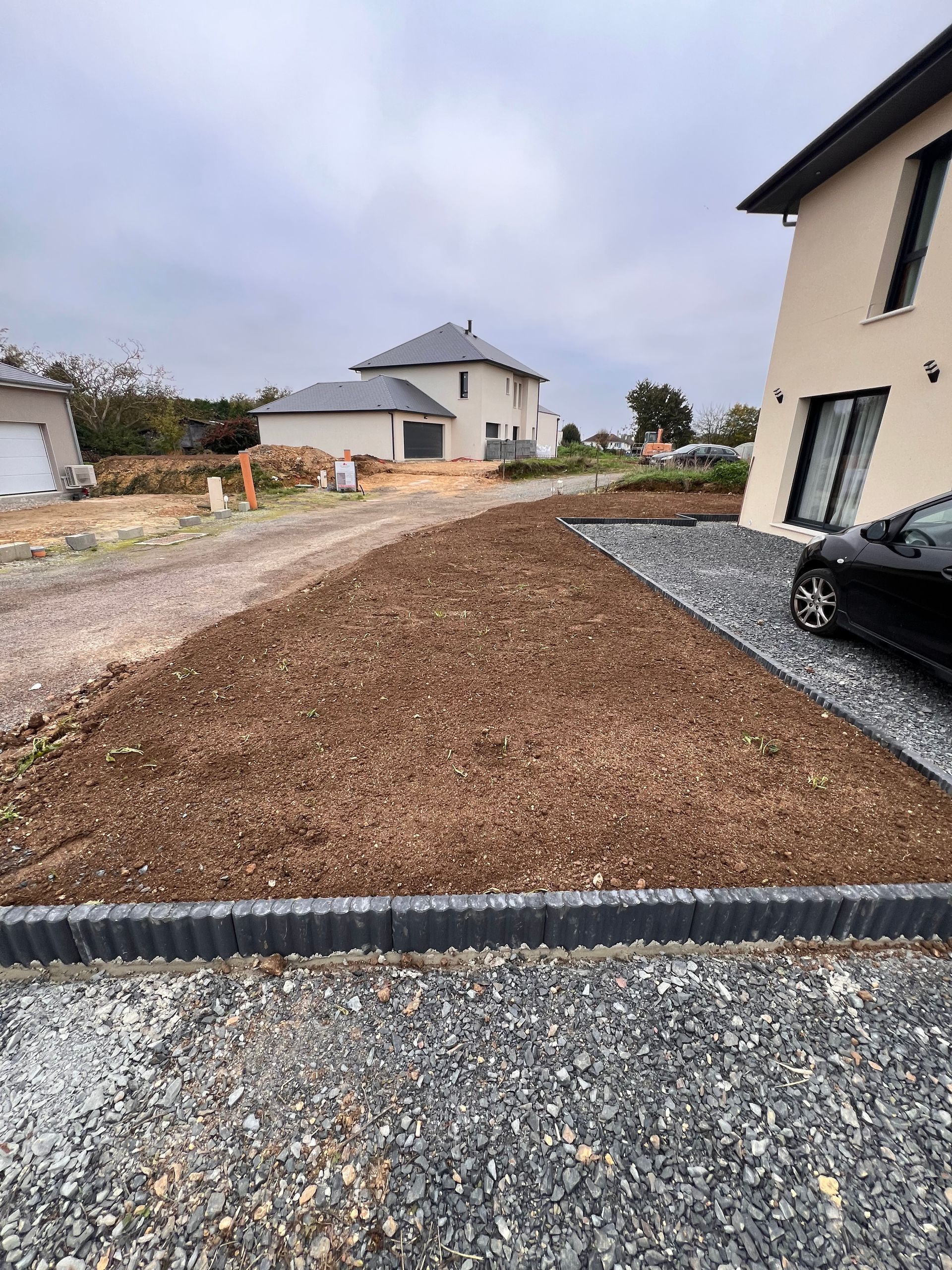 Petit jardin arrière avec pelouse verte, plantes en pot et tondeuse sur la droite. Vue sur une véranda en arrière-plan.
