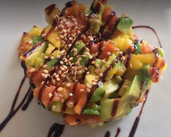 Un montículo de salmón, aguacate y mango cortados en dados, cubierto con semillas de sésamo y rociado con un glaseado balsámico oscuro.