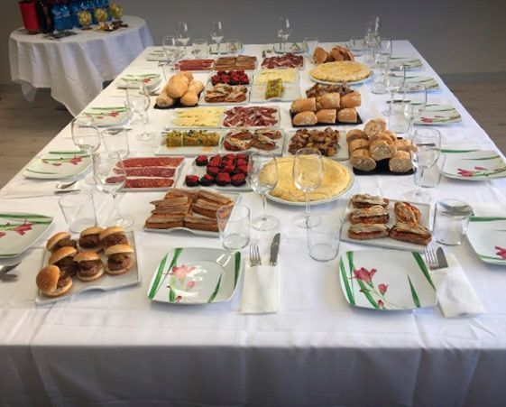 Una mesa larga preparada para un bufé con varios platos de comida, incluyendo panes, quesos, carnes y postres.