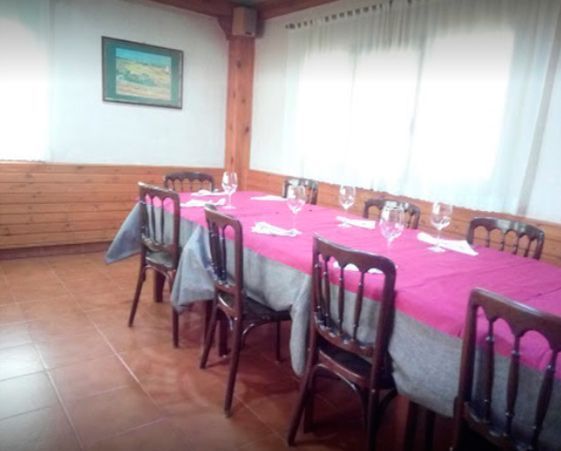 Un comedor con una mesa larga cubierta con un mantel rosa, rodeada de sillas de madera, preparada para una comida.