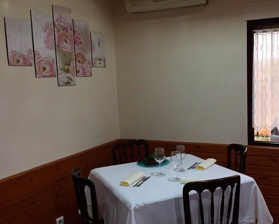 Una mesa de comedor con mantel blanco, cuatro sillas y vajilla, situada contra una pared revestida de madera y decorada con motivos florales.