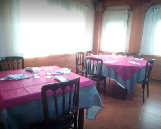 Dos mesas de comedor con manteles color magenta y sillas de madera en un luminoso salón de restaurante de estilo rústico.