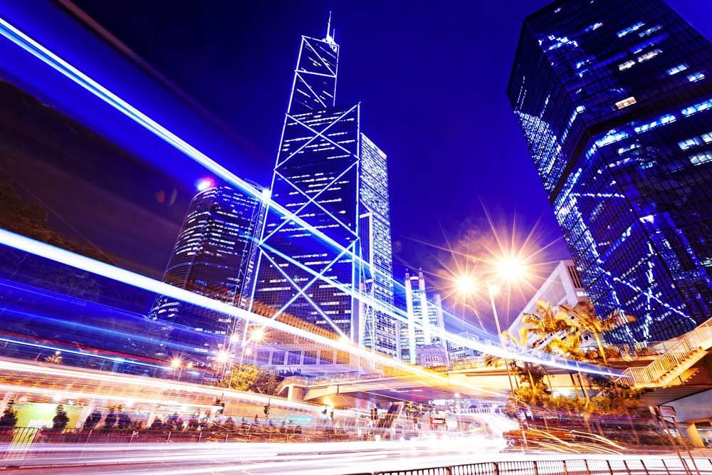 Vista nocturna desde un ángulo bajo de los rascacielos iluminados de Hong Kong con estelas de luz de larga exposición producidas por el tráfico.