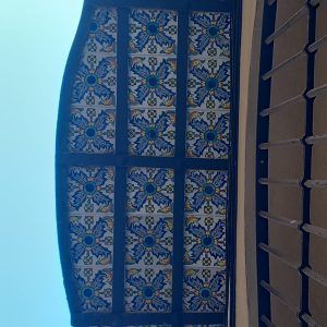 Ventana o panel de techo arqueado con estampado azul y azulejos decorativos junto a una pared de celosía de madera.