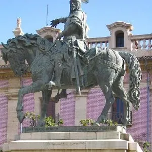 Estatua ecuestre de bronce sobre un pedestal frente a un edificio con azulejos rosas.