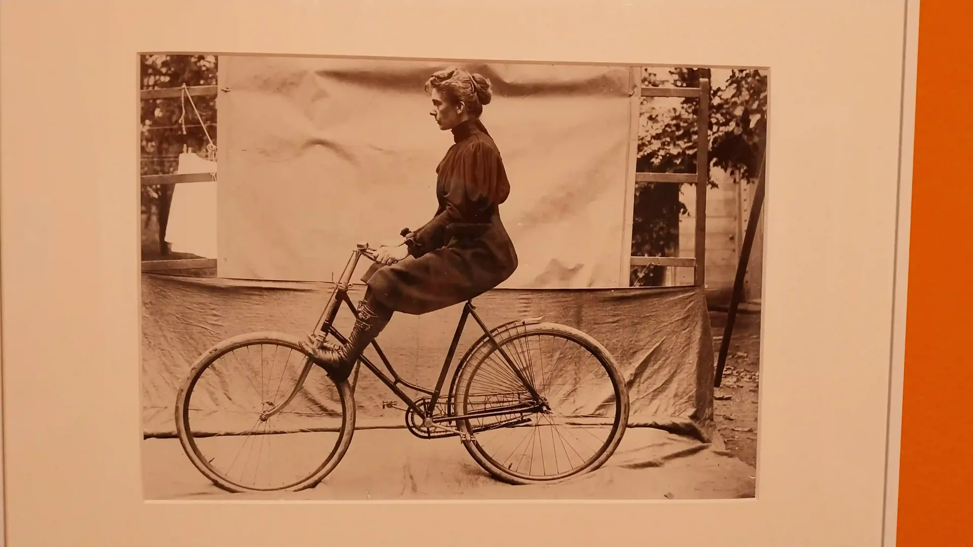 Fotografía en sepia de una persona sentada en una bicicleta al aire libre, con un fondo blanco y árboles detrás.