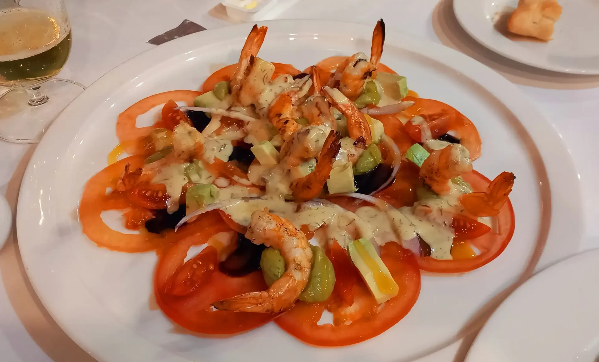 Ensalada de tomate y verduras emplatada con aderezo sobre un mantel blanco.