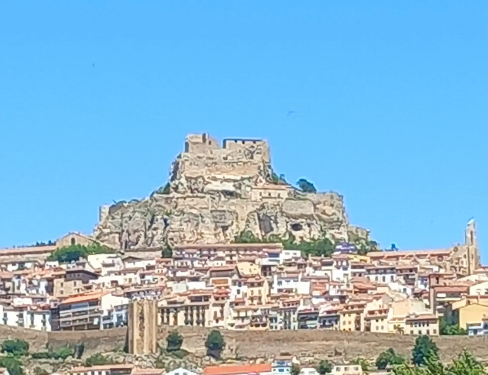 Castillo de piedra en la cima de una colina, sobre una densa ciudad, bajo un cielo azul despejado.