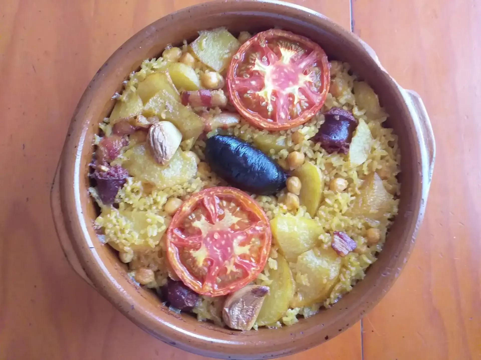 Un bol de cuscús con tomates cherry, aceitunas y nueces sobre una mesa de madera.