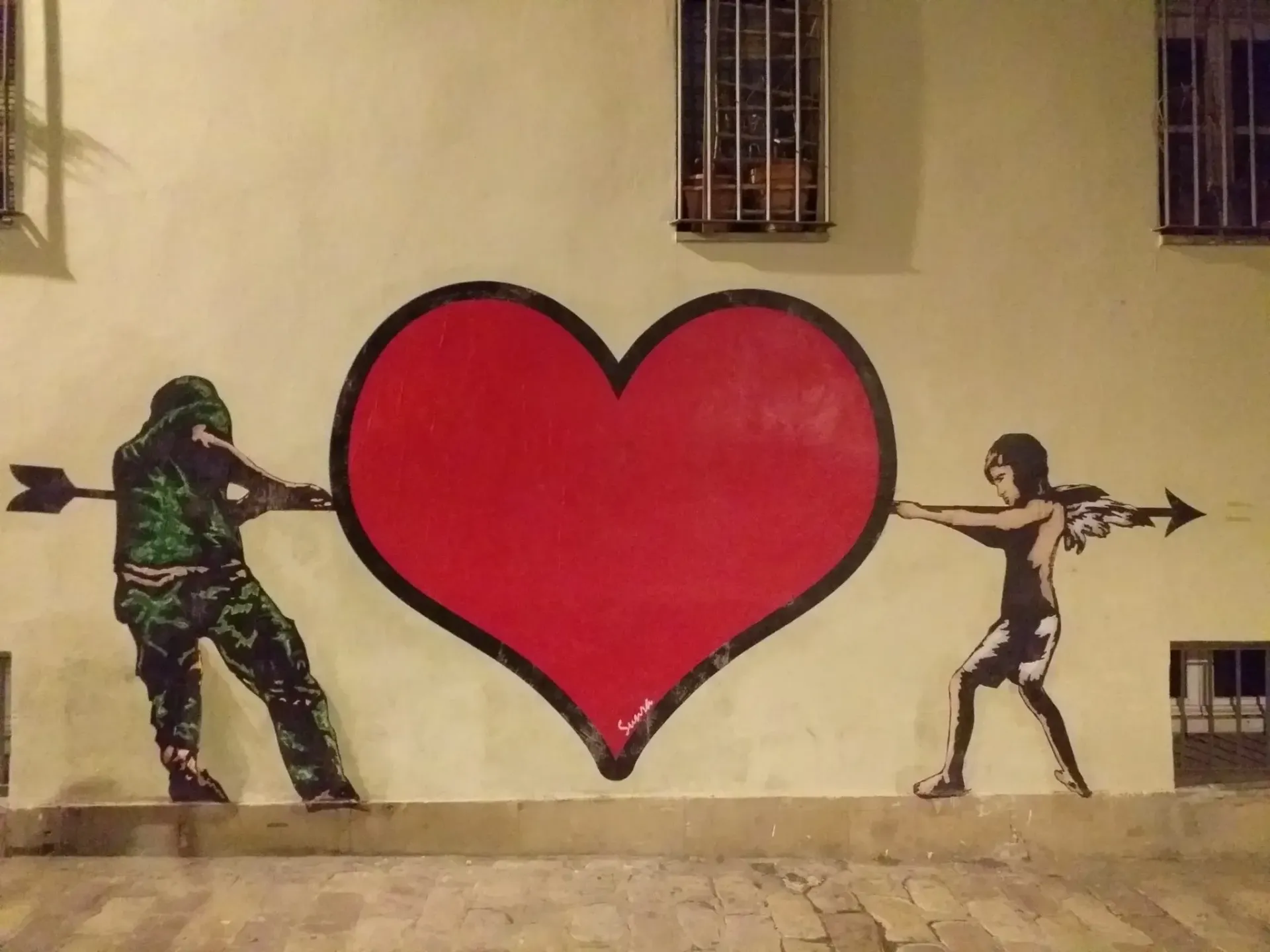 Mural de dos figuras separando un gran corazón rojo en una pared beige.