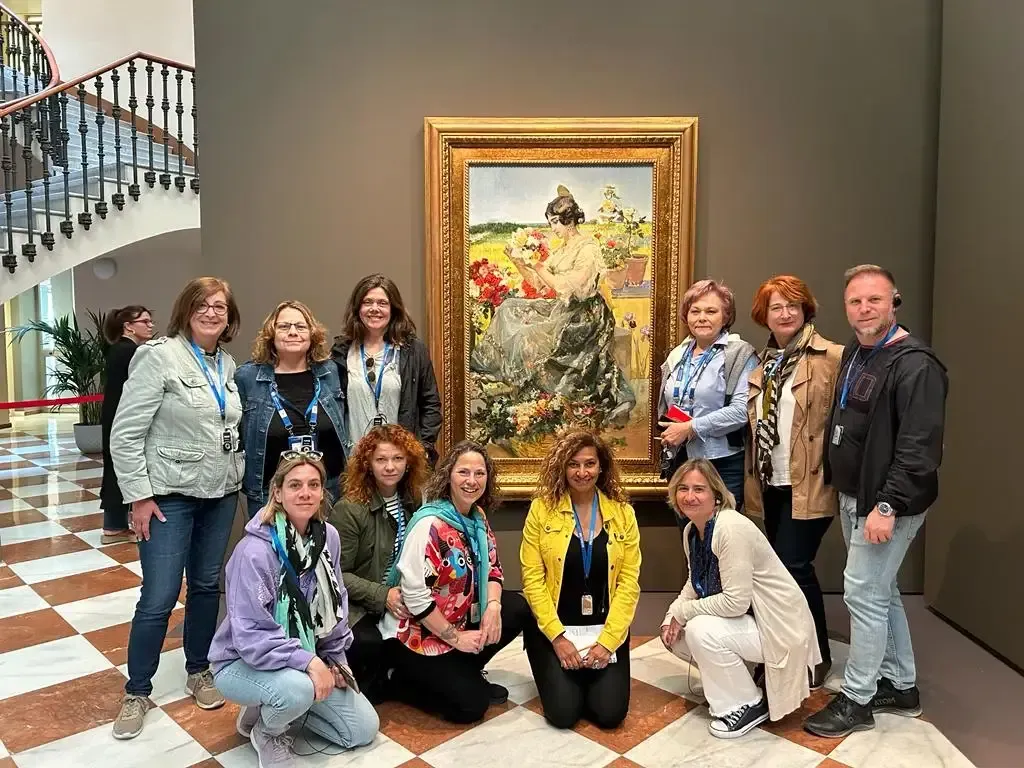 Grupo posando en una sala de un museo junto a un gran cuadro floral enmarcado.
