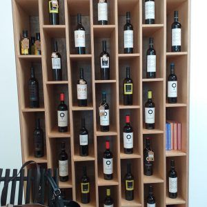 Botellero de madera lleno de botellas de vino variadas en una habitación con suelo de baldosas.