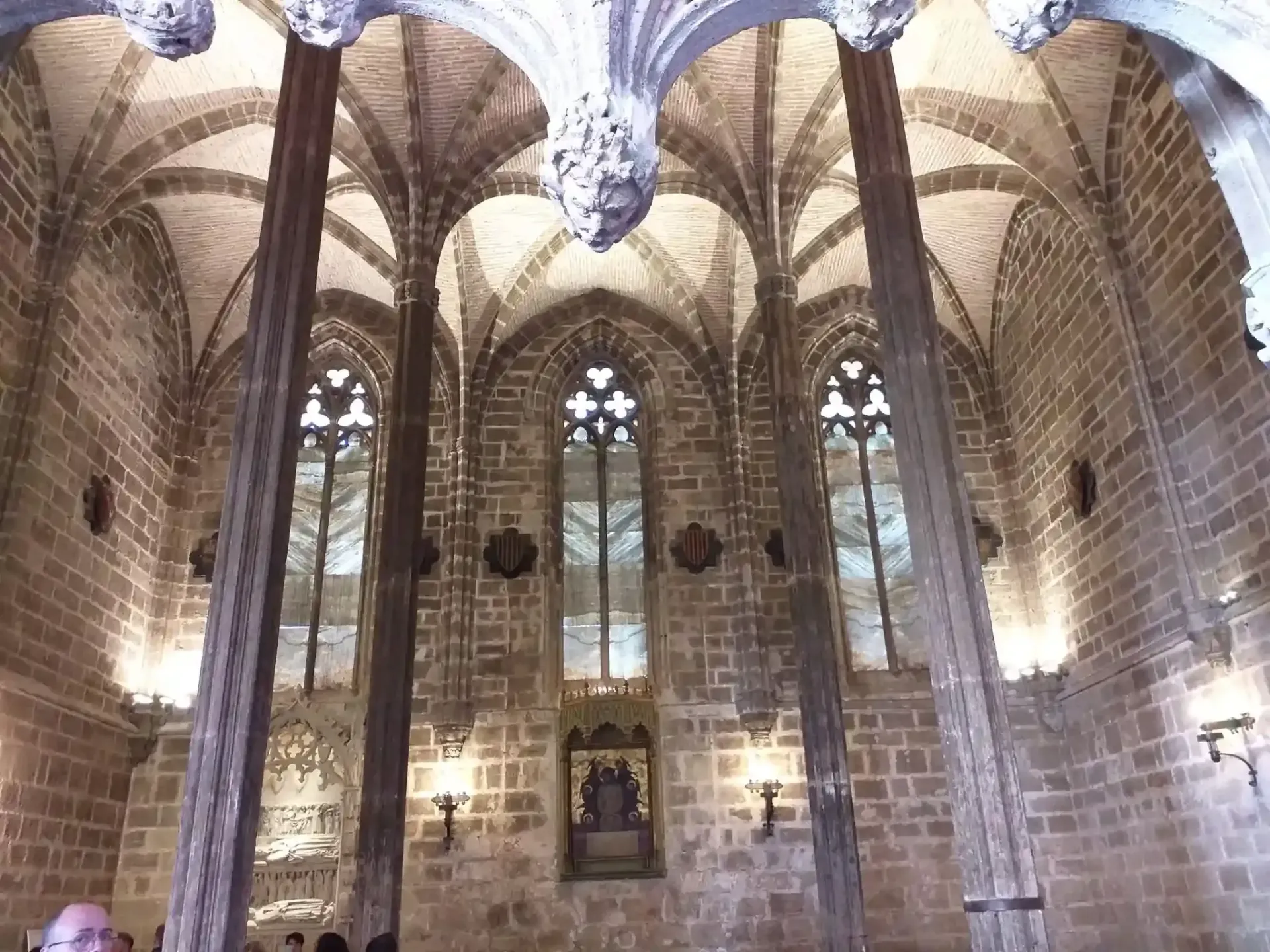 Interior de iglesia de piedra con techo abovedado, ventanas arqueadas y una lámpara de araña colgante.
