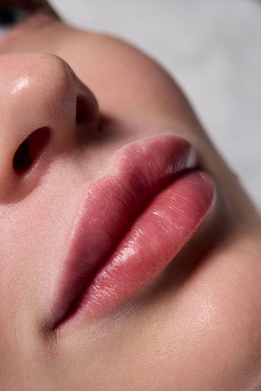 Gros plan sur des lèvres roses brillantes et une partie du nez sur un fond neutre et doux
