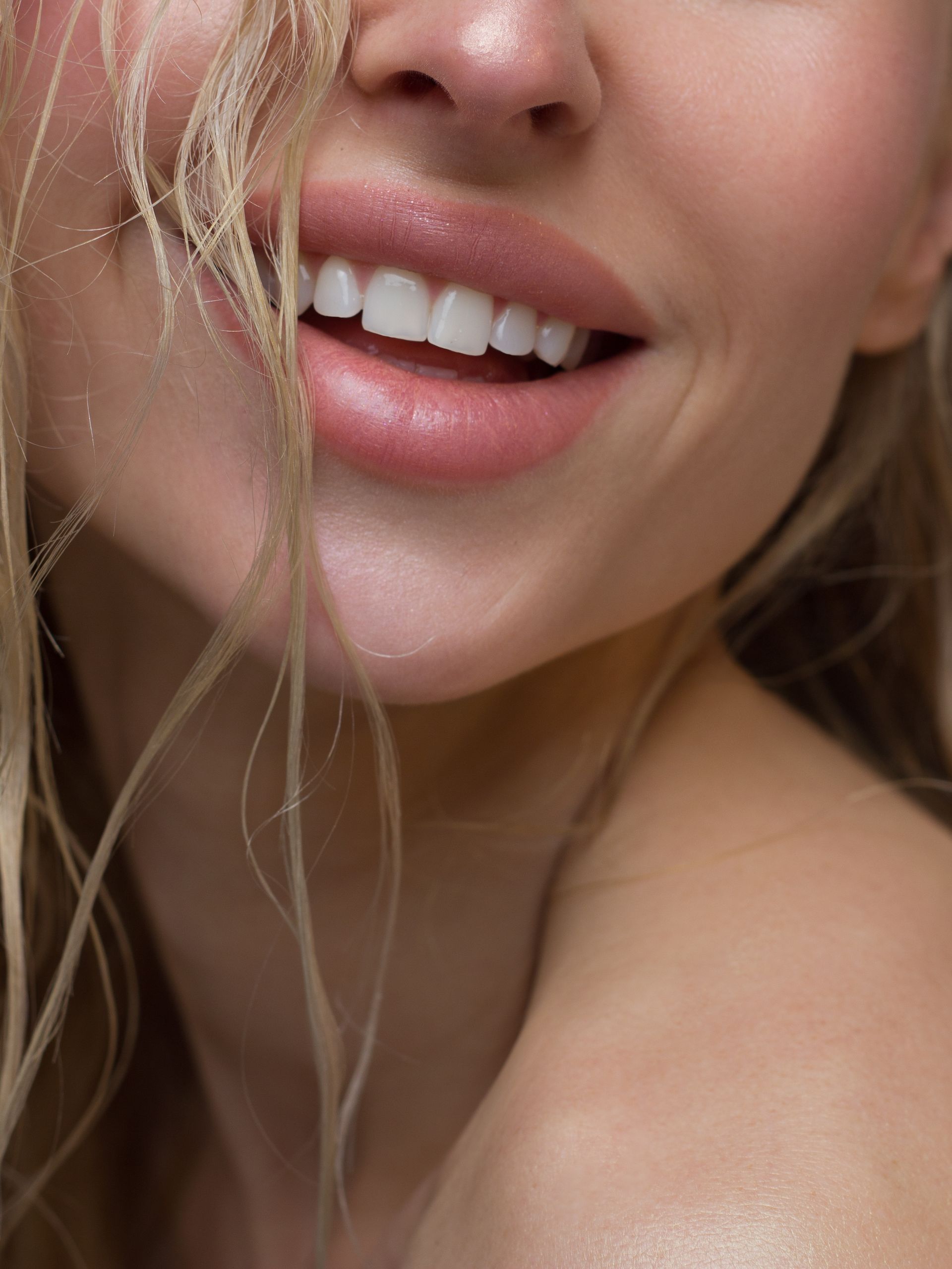 Gros plan sur un visage souriant, cheveux blonds et épaule dénudée, sur fond doux.
